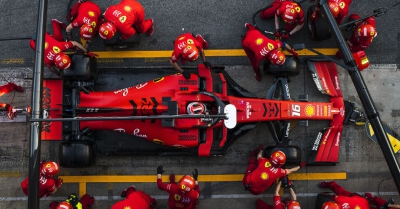 A red formula one race car photographed from above while a team work on its tyres