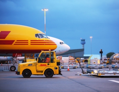 A yellow plane, and yellow DHL cart in a busy airport