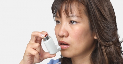 A woman's face, she is holding a white inhaler up to her mouth