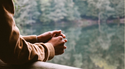 A pair of hands clasped with a blurred tree and lake background