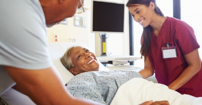 a lady in a hospital bed smiles up at two healthcare professionals