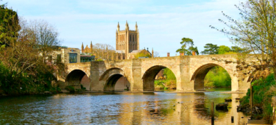 A four arched bright over a river with a cathedral building in the distance