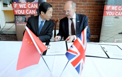 Sir John Peace and Governor Xu talking over a signed document with British and Chinese flags in front on a table