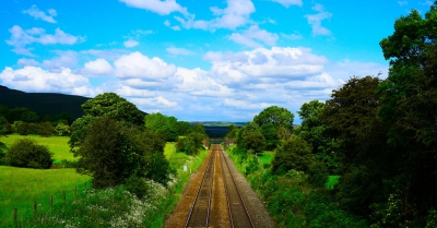 a train track leading into the distance with green fields and trees all around